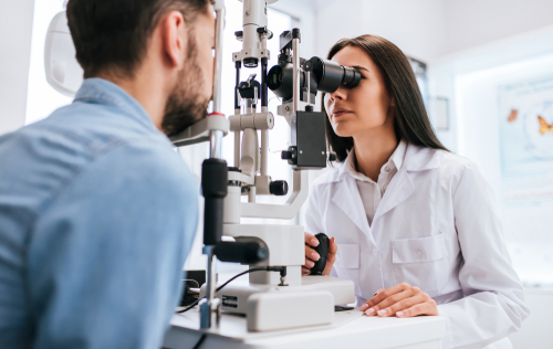 An optometrist conducts an eye exam on a male patient, providing services supported by the best vision insurance brokers in Oklahoma.