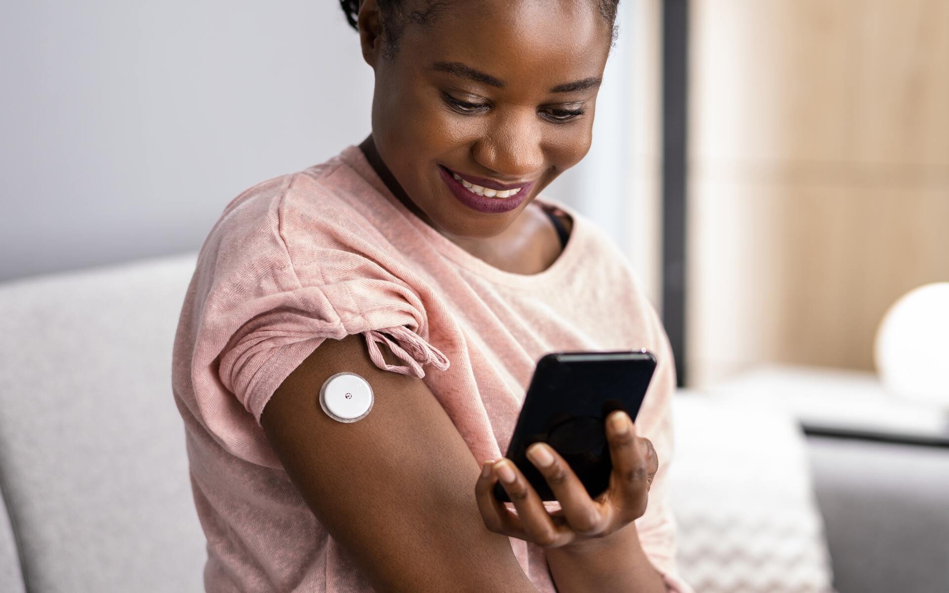 ok.vision A woman using a smartphone for remote patient monitoring while wearing a medical device on her arm.