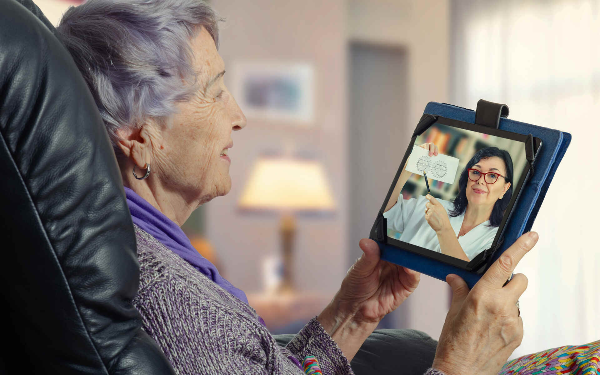 An elderly woman engaging in a telehealth consultation via a tablet with a medical professional explaining a diagram.