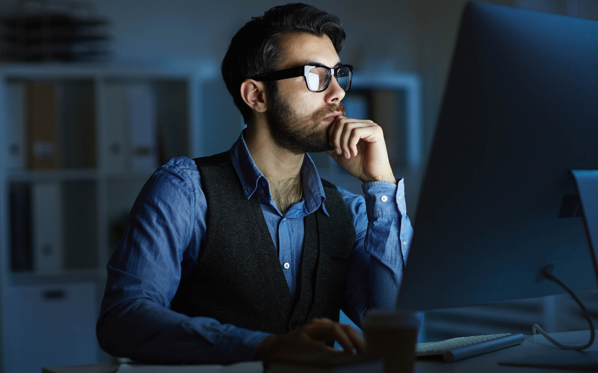 Qmerit vision benefits A man wearing glasses works late at a computer, emphasizing the importance of vision benefits for screen users.
