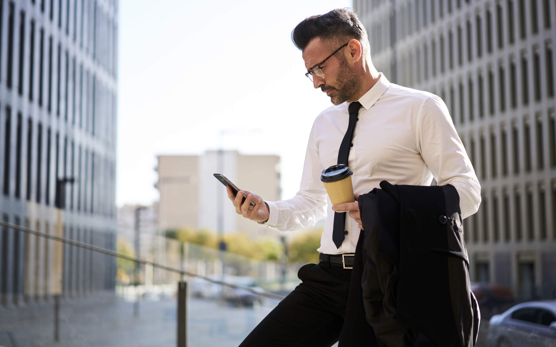 VCD best vision plans for brokers A business professional in a white shirt and black tie checks his phone while holding coffee, possibly researching the best vision plans for brokers.