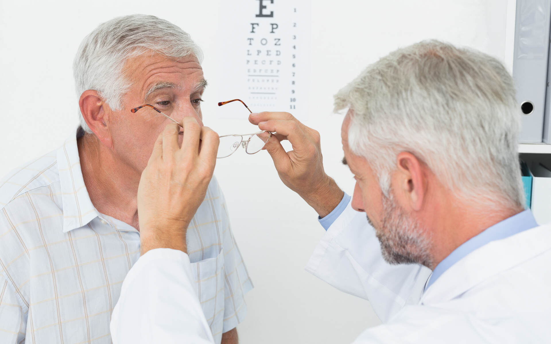An optometrist helps an elderly man try on glasses during an eye exam as part of vision care plans.