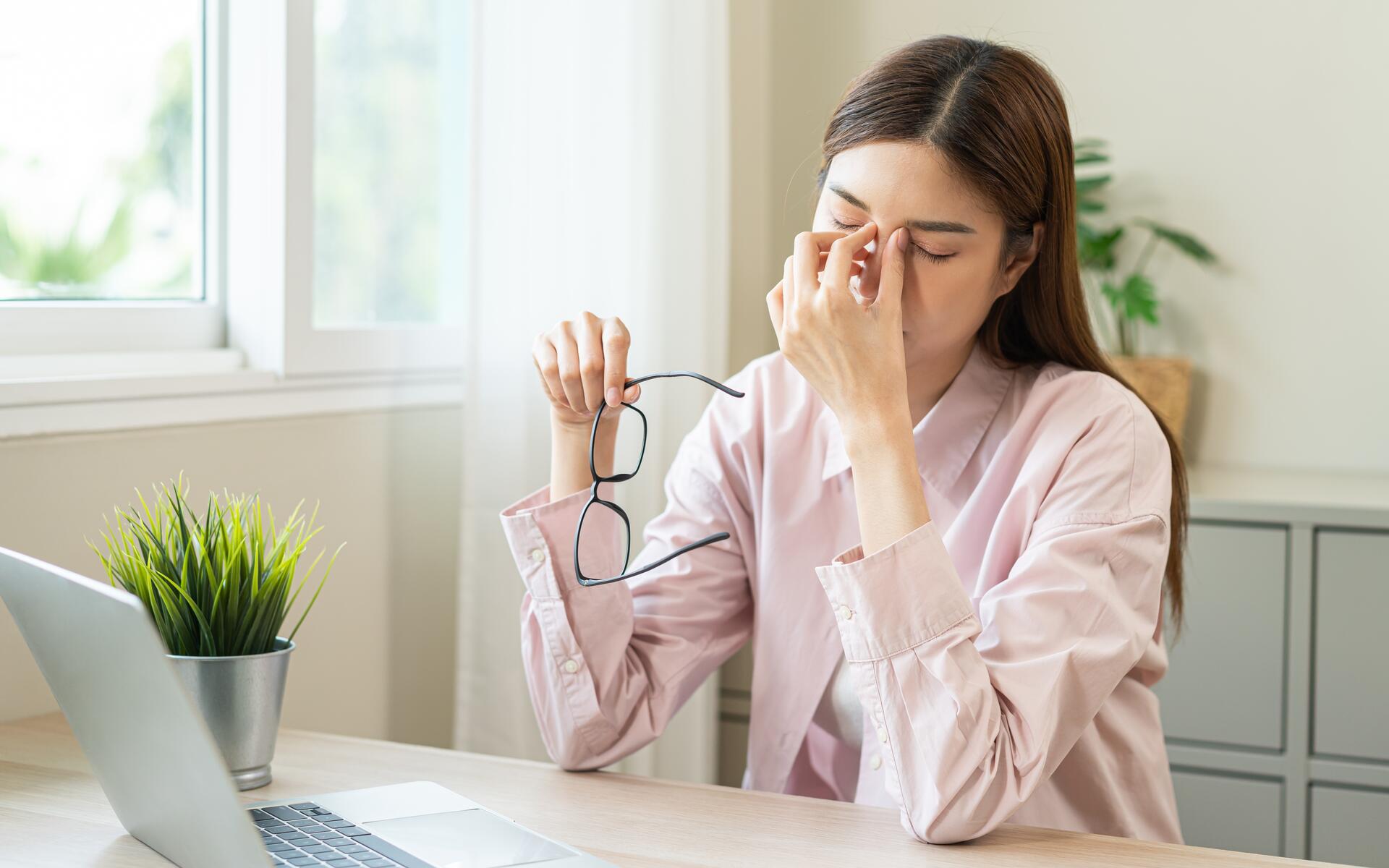 A woman experiencing eye strain at her desk, highlighting the importance of vision benefits for small businesses.